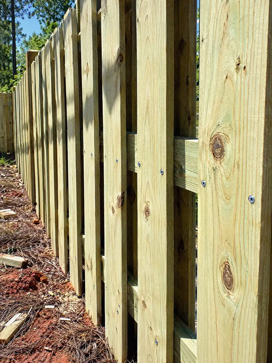 Close view along a shadowbox fence with boards on both sides of the rail and small gaps between them